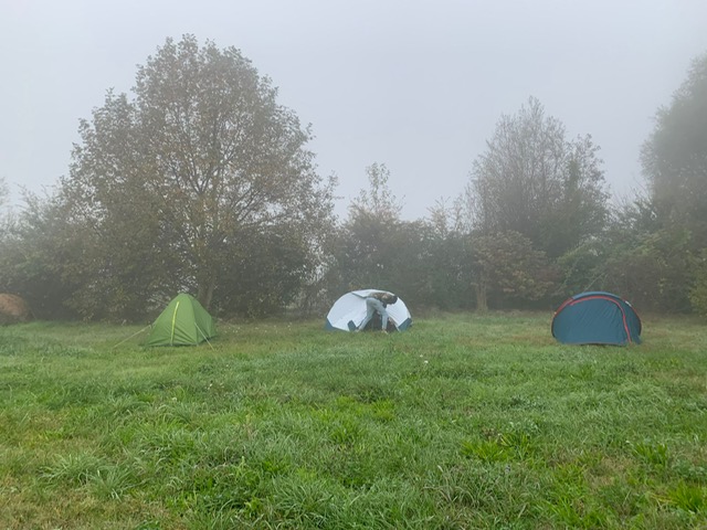 Drie tenten opgezet op een mistig grasveld met bomen op de achtergrond