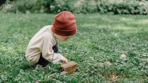 Kind met rode muts onderzoekt de natuur in de tuin, kijkend naar een steen